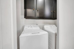 A laundry room with two white front-loading washing machines and a dark wooden cabinet above them. - Main Street Retreat in Roseville (Roseville)