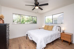 A bedroom with a bed, two bedside tables, a dresser, and a ceiling fan. There are two windows providing natural light. - Main Street Retreat in Roseville (Roseville)