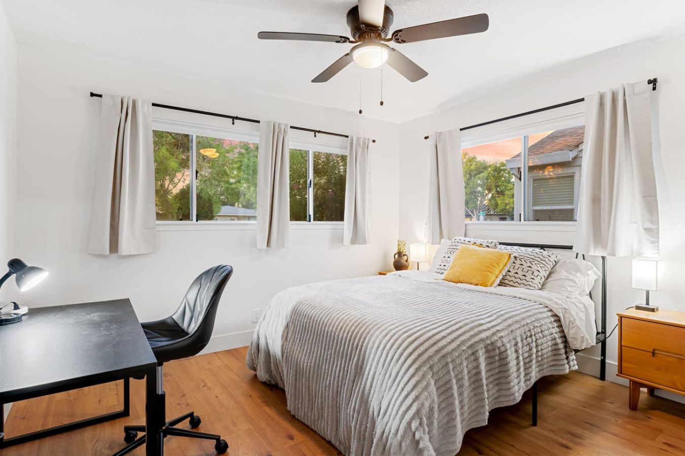 A bedroom with a bed, desk, chair, and a ceiling fan.