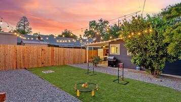 Un jardin avec une pelouse artificielle, un trampoline, un espace barbecue et une clôture en bois.