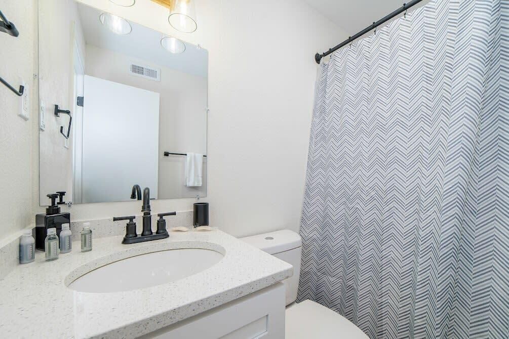 A bathroom with a white sink, black faucet, and a mirror above it. There is a toilet visible in the background.