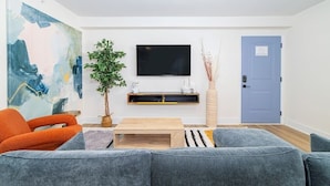 Ett modernt vardagsrum med en grå soffa, en orange fåtölj och en platt-TV som är monterad på väggen.