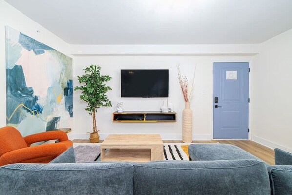 Uma sala de estar moderna com um sofá cinzento, uma poltrona laranja e uma TV de tela plana presa na parede.