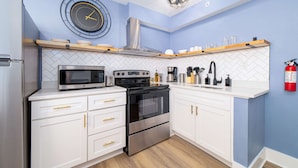A modern kitchen with white cabinetry, a stainless steel oven, a microwave, and a clock on the wall.