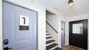 Ein Flur mit einer blauen Tür, auf der “Tide Suite 1” steht, einer Treppe und einer schwarzen Tür mit der Nummer 2.