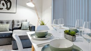 A modern living room with a sofa, a dining table set with plates, bowls, and wine glasses, and a floor lamp.