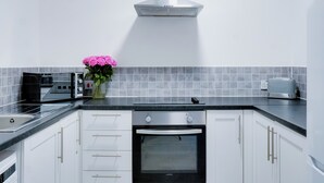 A modern kitchen with white cabinets, a black oven, a stainless steel range hood, and a toaster on the countertop.