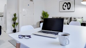 A modern, minimalist room with a white table, a laptop, a pair of glasses, and a white mug.