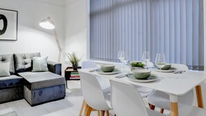 A modern living room with a sectional sofa, dining table set for four, and a large window with blinds.