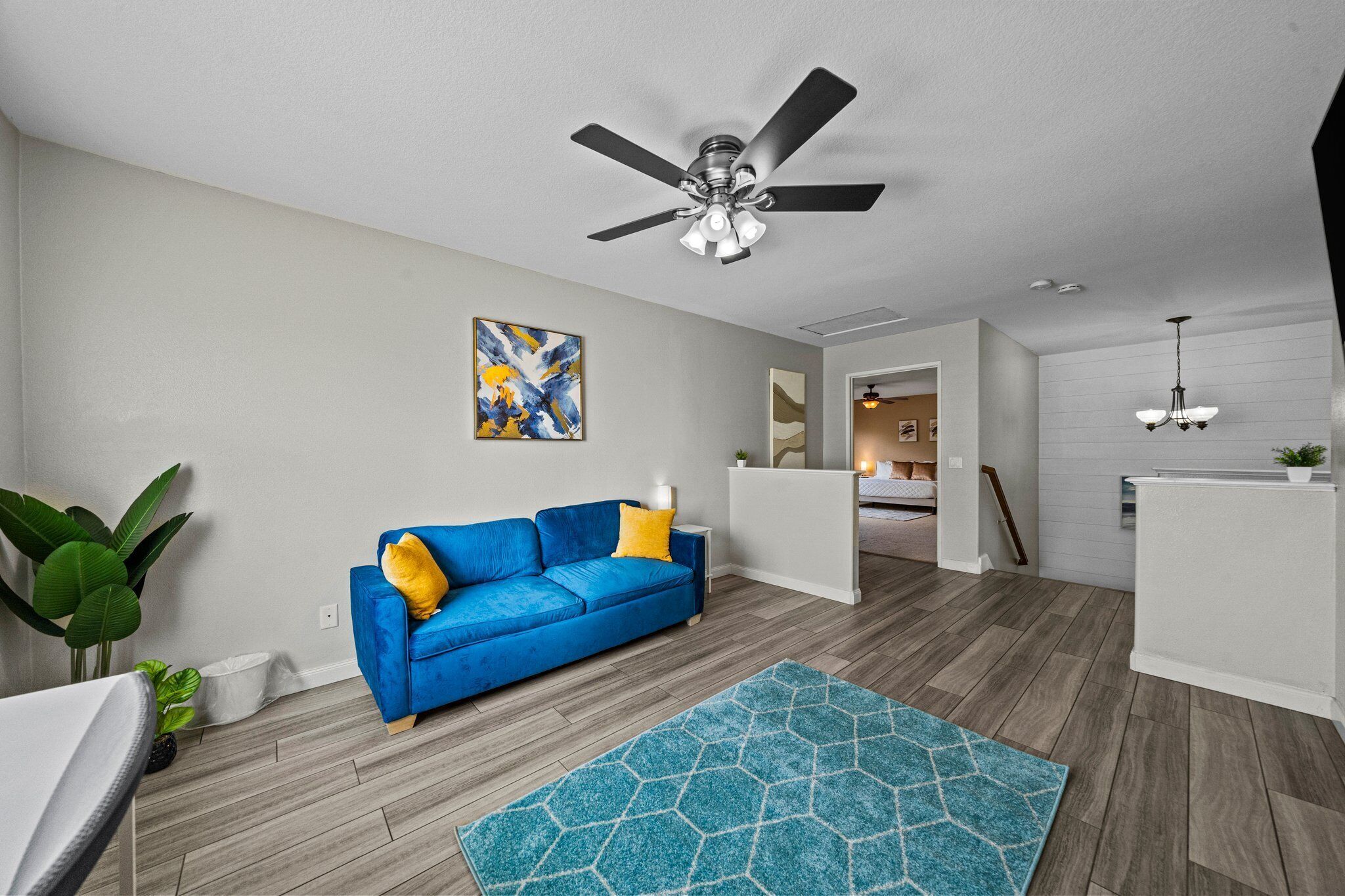 A modern living room with a blue sofa, a ceiling fan, and a geometric rug.