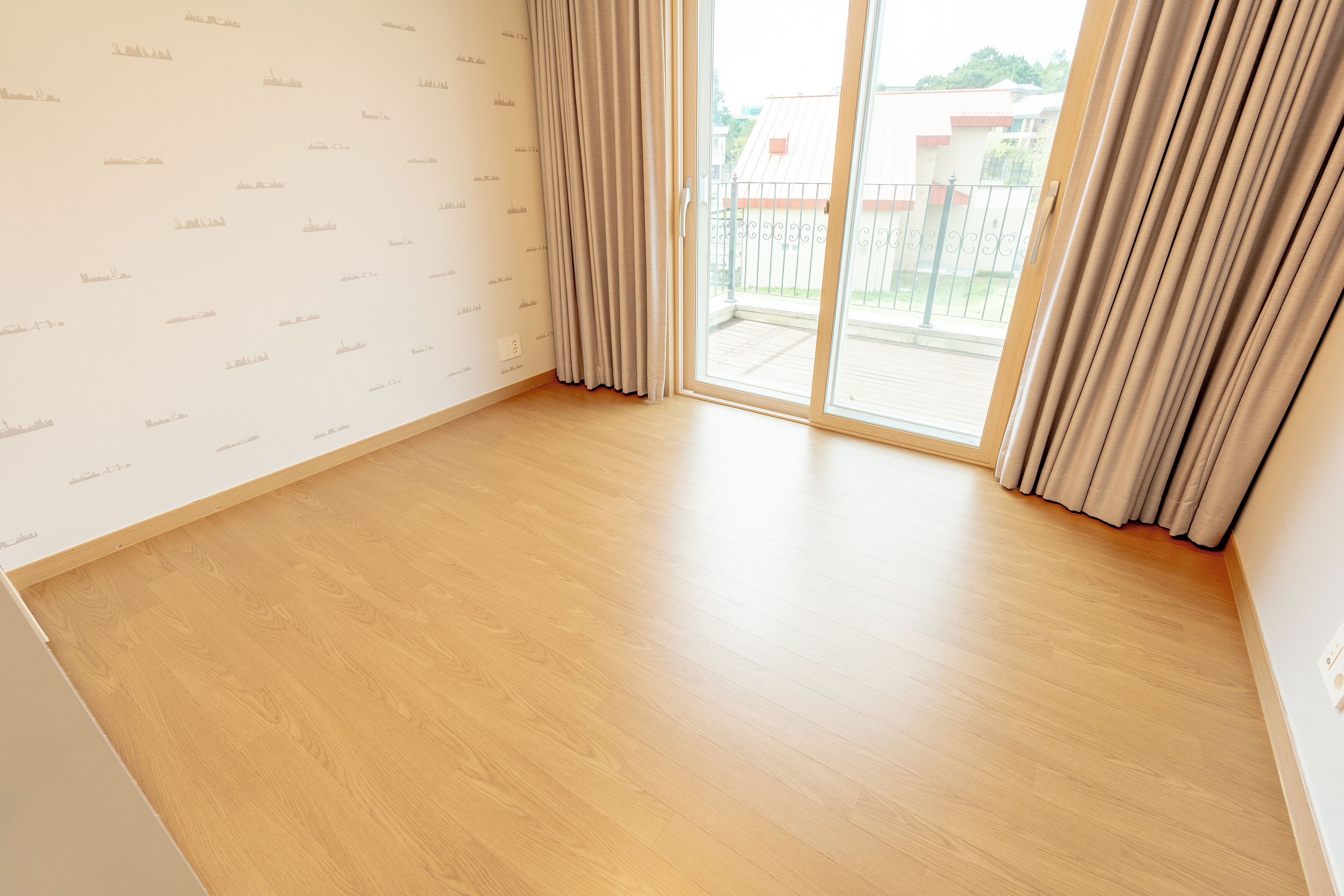 Une pièce dotée d’un plancher en bois, d’une porte-fenêtre coulissante donnant sur l’extérieur et d’un mur sobre orné d’un motif répétitif.