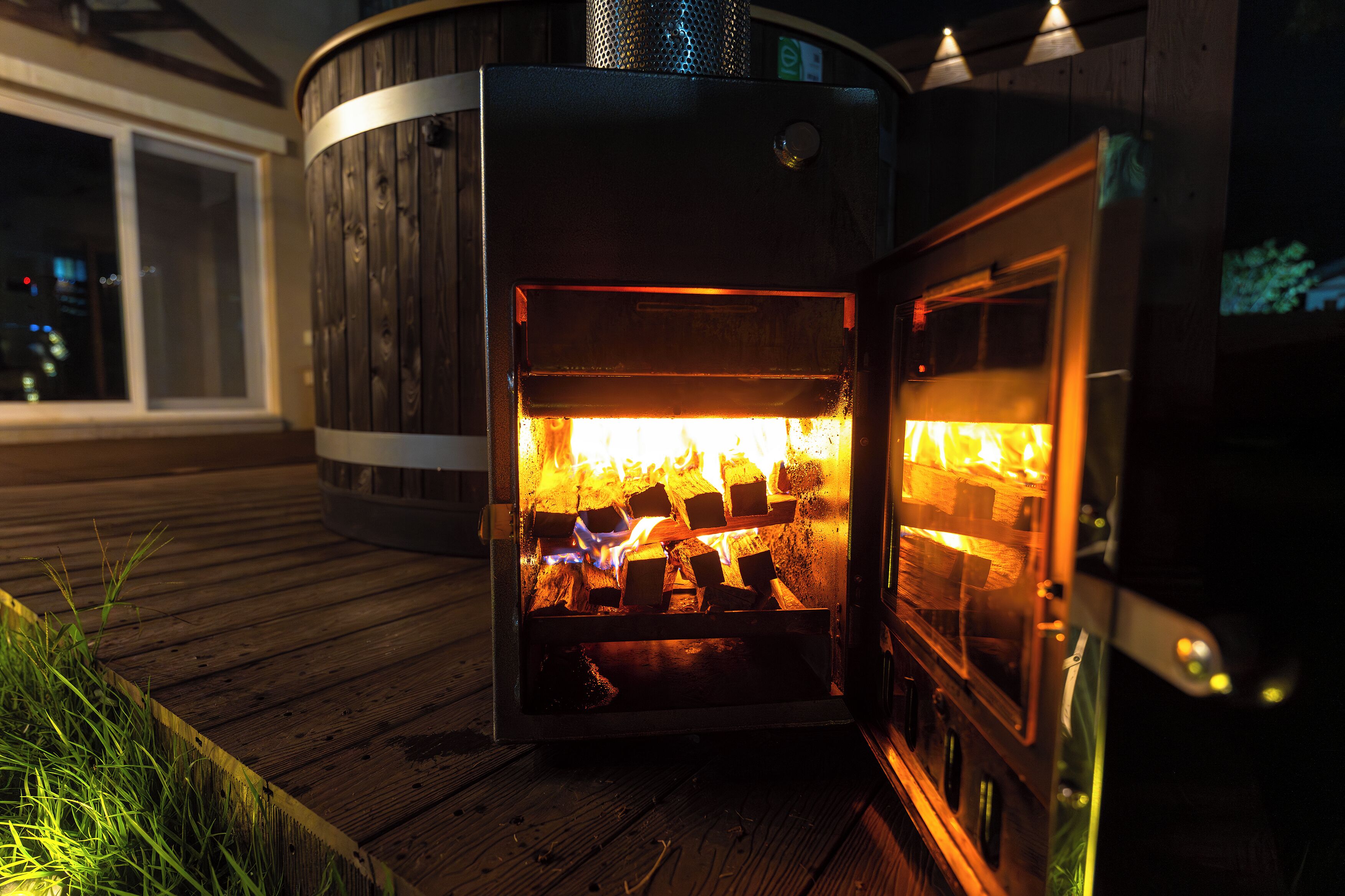 Un poêle à bois avec des bûches apparentes à l’intérieur, installé sur une terrasse en bois.