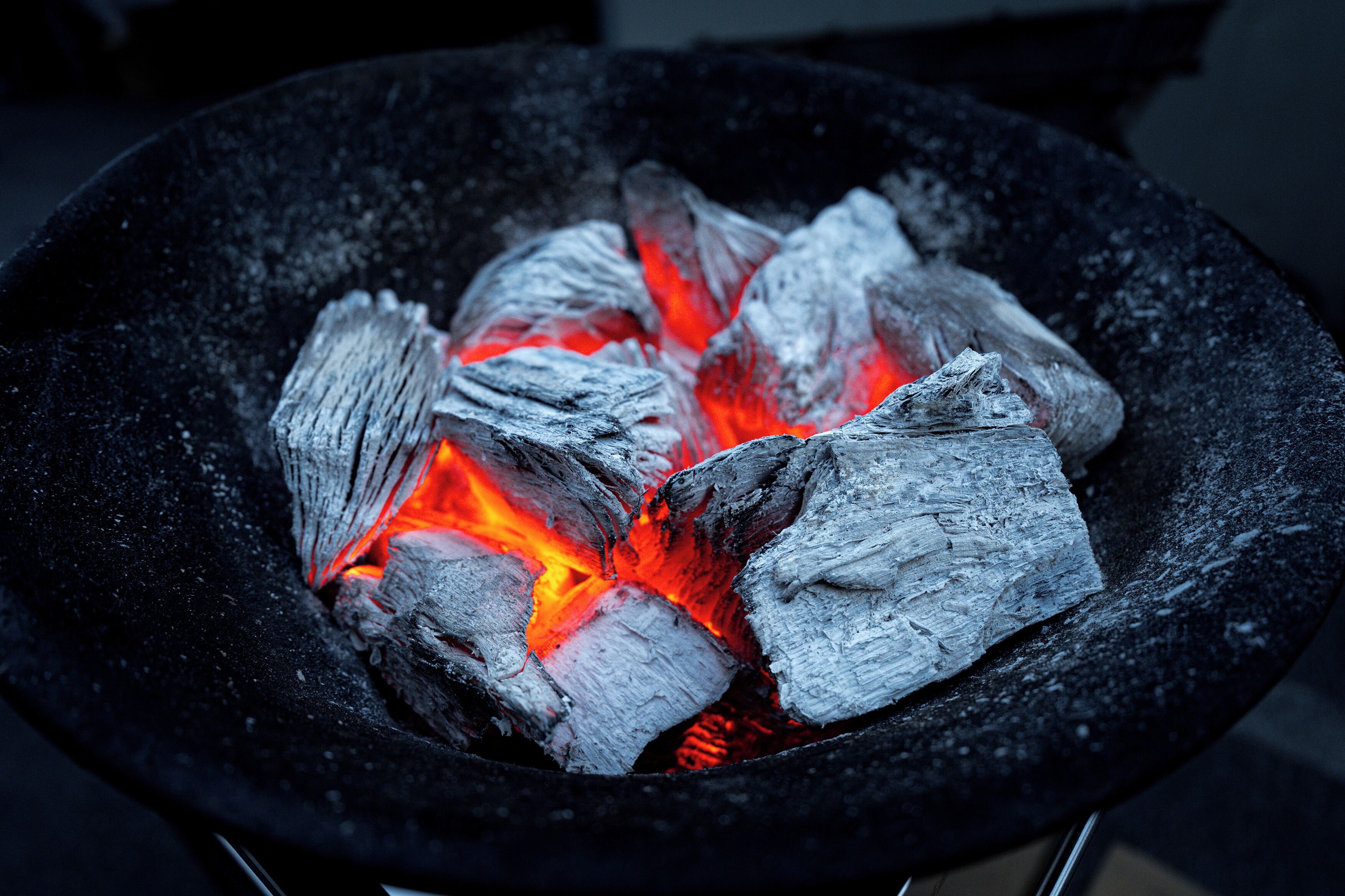 Gros plan sur du charbon de bois en combustion dans un barbecue noir.