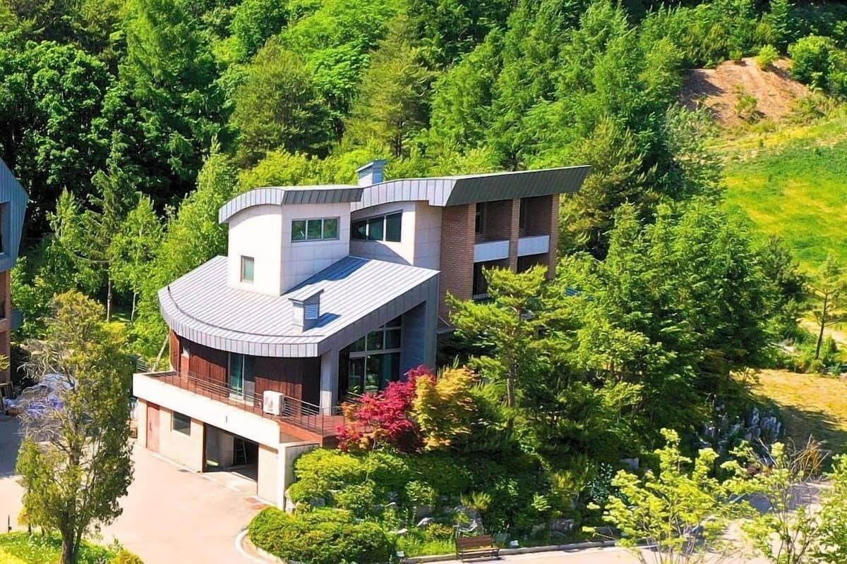 A modern two-story building with a curved roof, surrounded by dense greenery and trees.