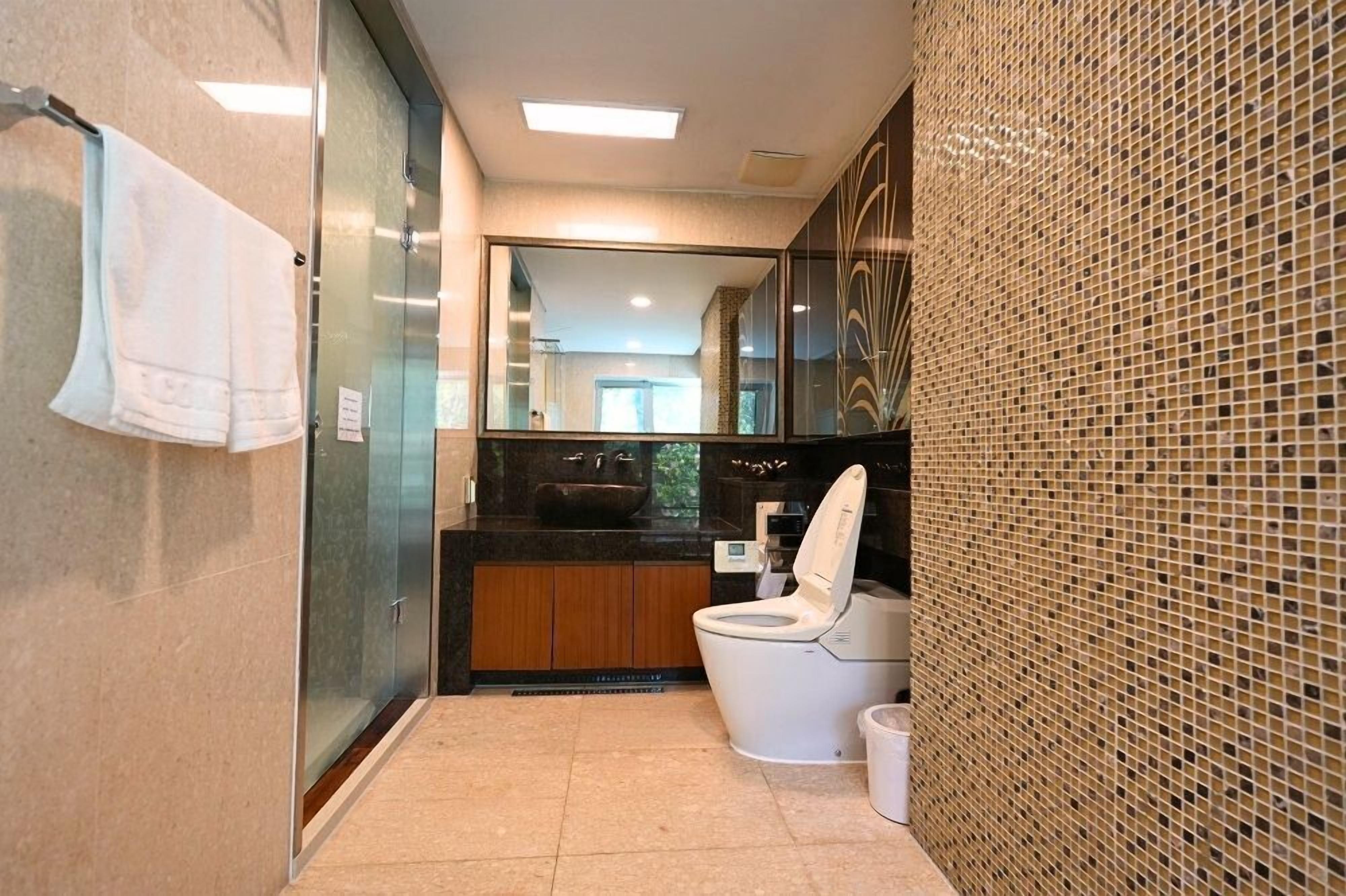Un baño moderno con cabina de ducha de vidrio, inodoro blanco y un espejo grande.