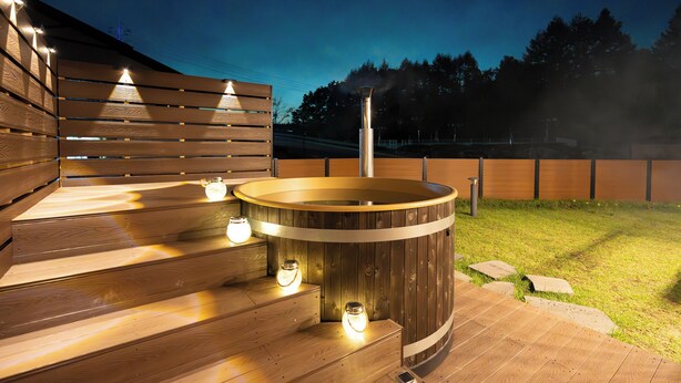 Un bain à remous doté d’un escalier et d’un éclairage en bois, entouré d’une terrasse en bois et d’une zone herbeuse.