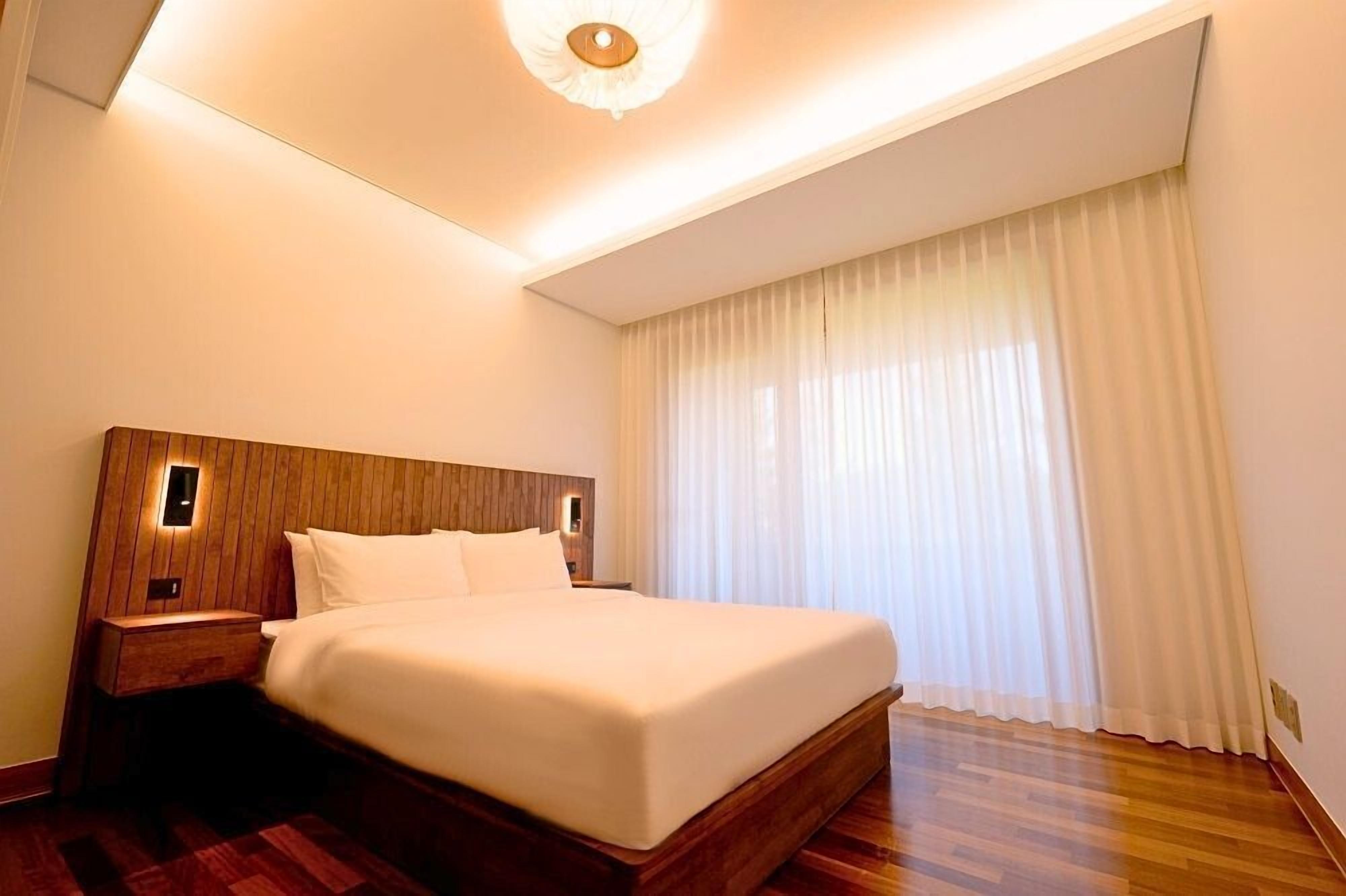 A hotel room with a large bed, wooden headboard, bedside tables, and a ceiling light fixture.
