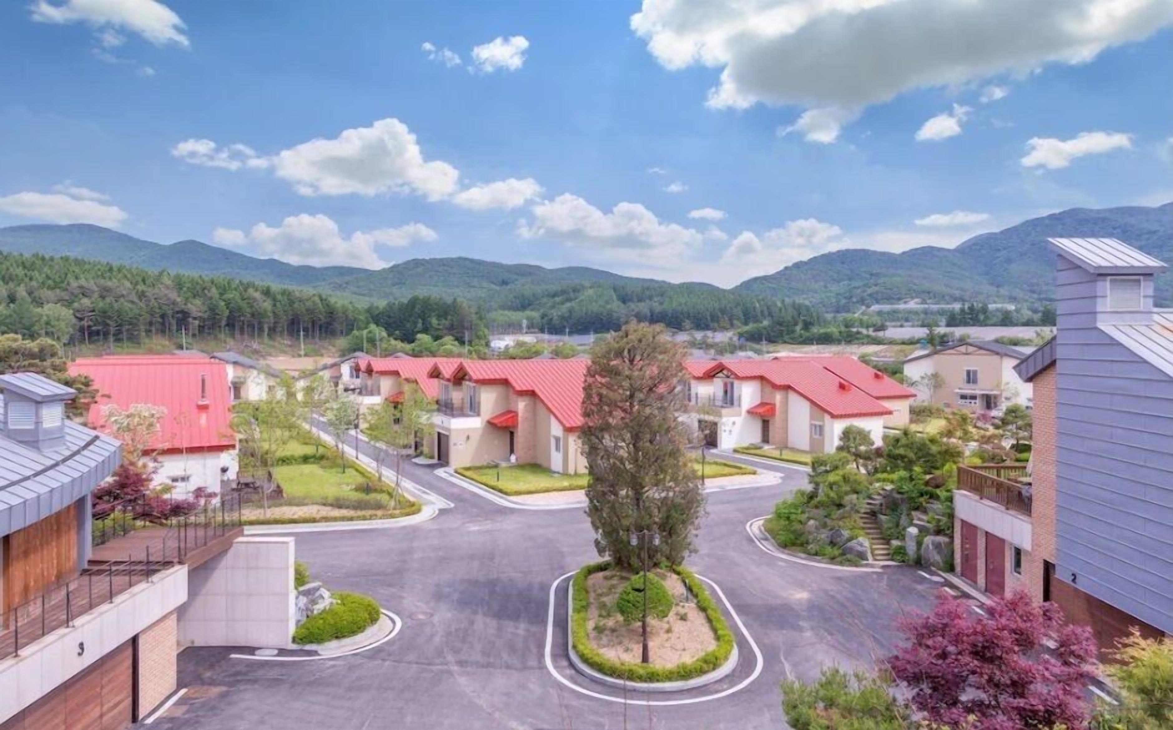 Zona residencial con casas de tejados rojos, rodeada de vegetación y montañas al fondo.