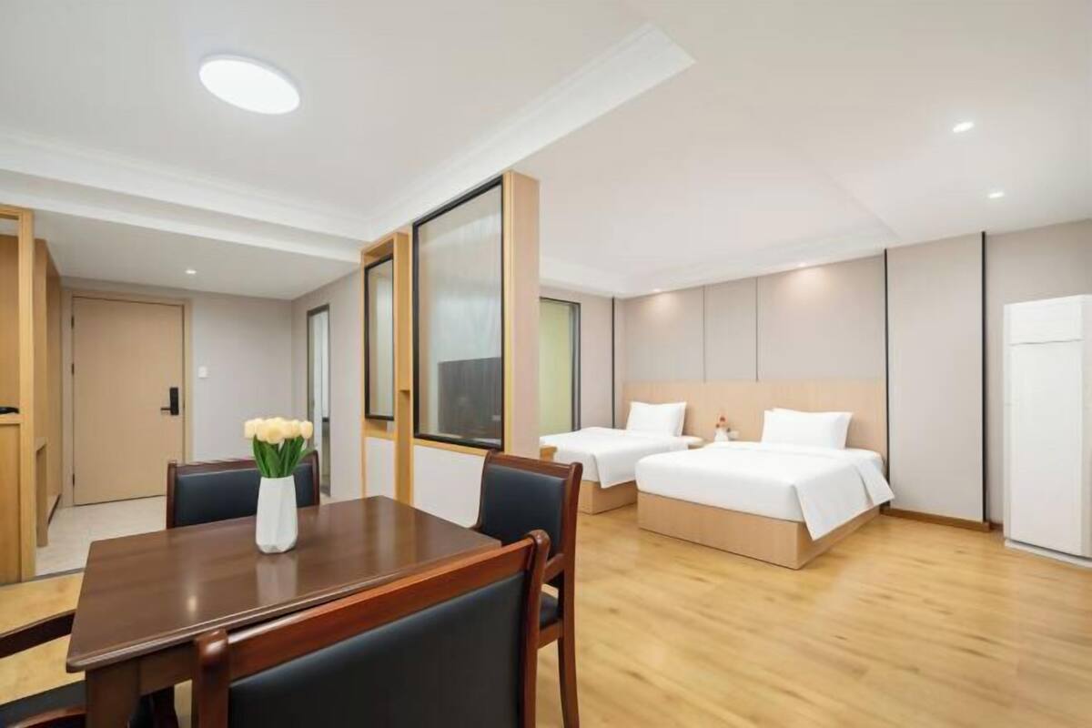A hotel room with a wooden dining table, two beds, and a large window.