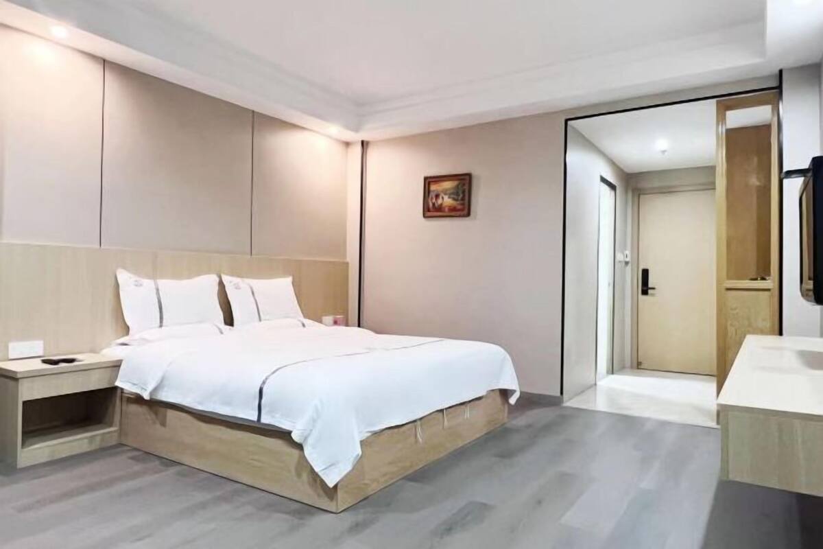 A modern hotel room with a large bed, bedside tables, a small desk, and a bathroom visible through an open door.