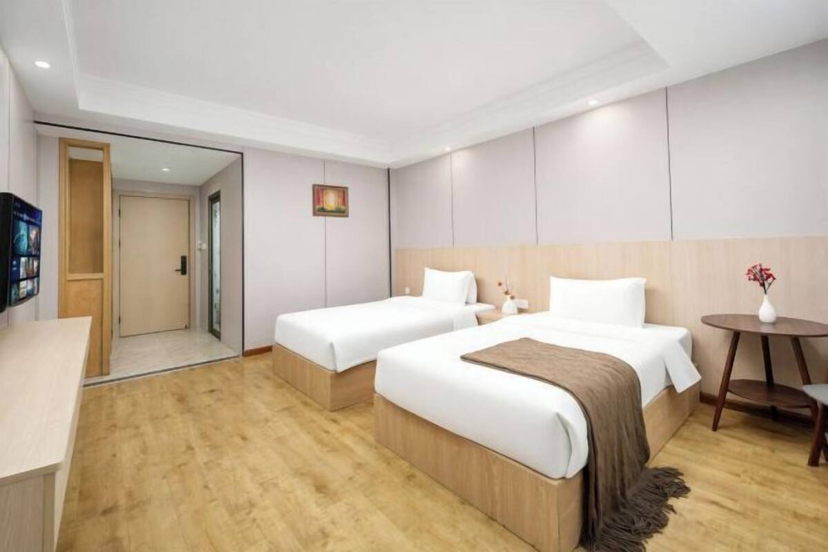 A hotel room with two beds, a small table, a TV, and a door leading to another room.