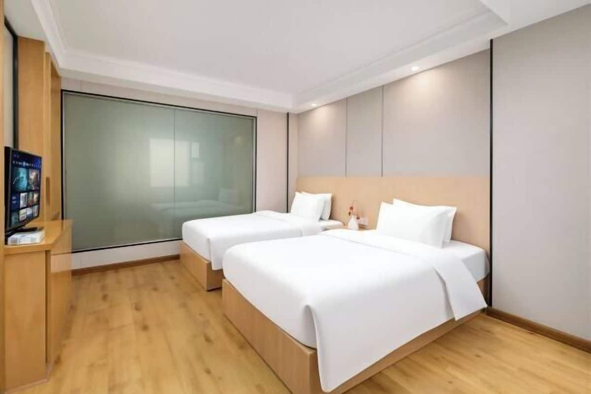 A hotel room with two beds, a wooden floor, a large window, and a flat-screen TV on a wooden stand.