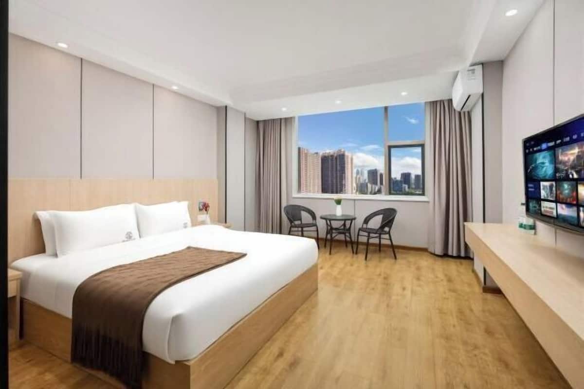 A hotel room with a large bed, a desk with two chairs, a television, and a window with a city view.