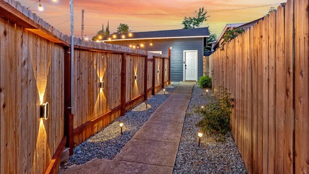 A wooden fence-lined pathway leading to a small building with a door, string lights, and a gravel path. - Studio on Main Street  (Roseville)