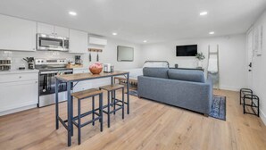 A modern kitchen with white cabinets, a stainless steel stove, and a dining area with a wooden table and stools. - Studio on Main Street  (Roseville)