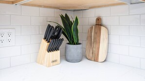 A kitchen with white tiles, a knife block, a potted plant, and a wooden cutting board. - Studio on Main Street  (Roseville)