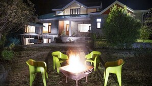 A house with a fire pit in the yard, surrounded by green chairs.
