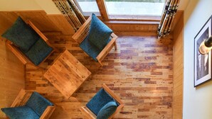 A wooden interior with a sloped ceiling, four wooden chairs with cushions, and a large window.