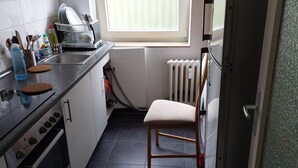 Una cocina compacta con estufa, fregadero y una silla cerca de la ventana.