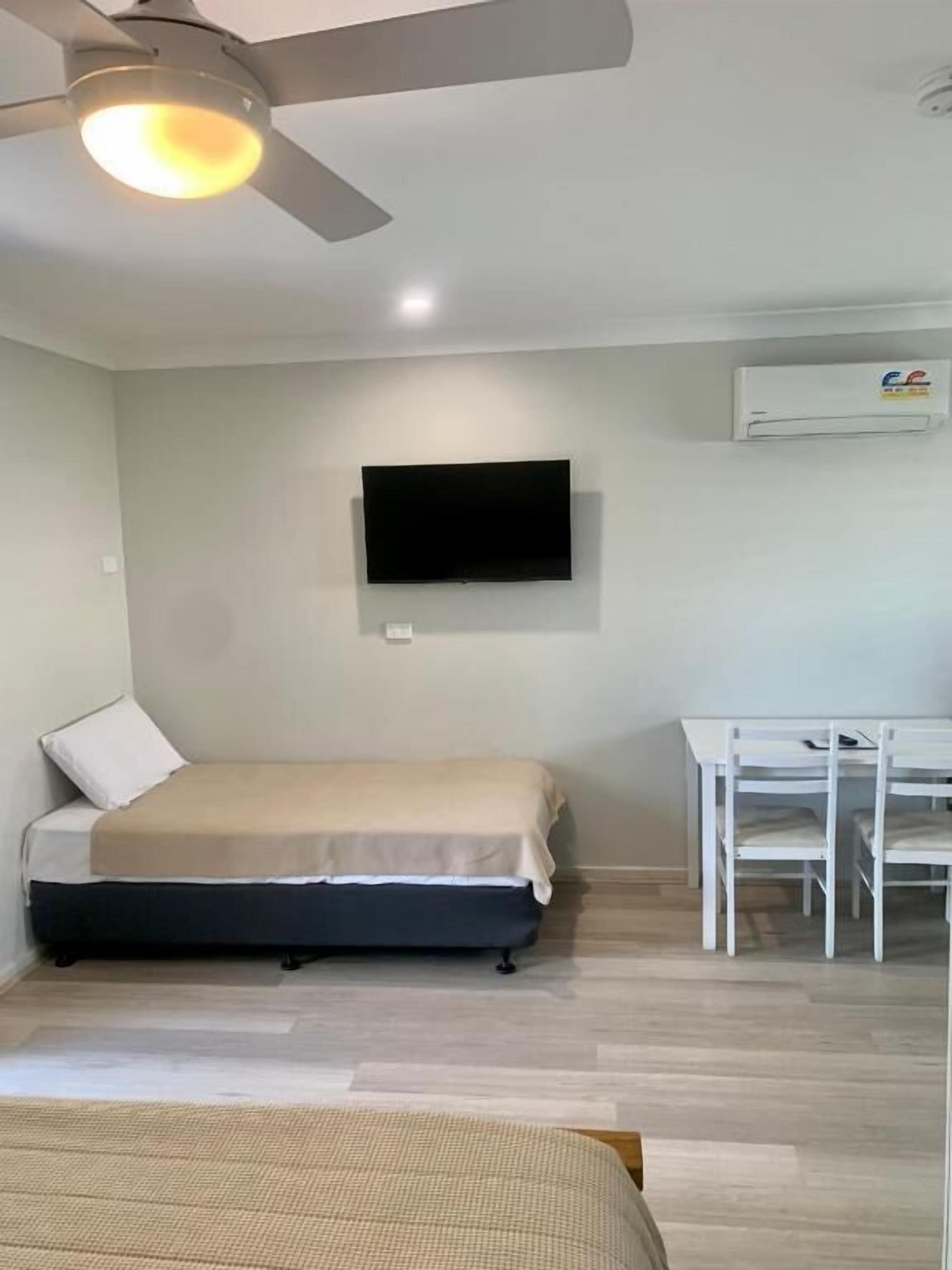 A bedroom with a bed, a desk, a ceiling fan, and a mounted TV.
