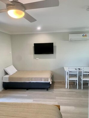 Een slaapkamer met een bed, een bureau, een plafondventilator en een tv aan de muur.