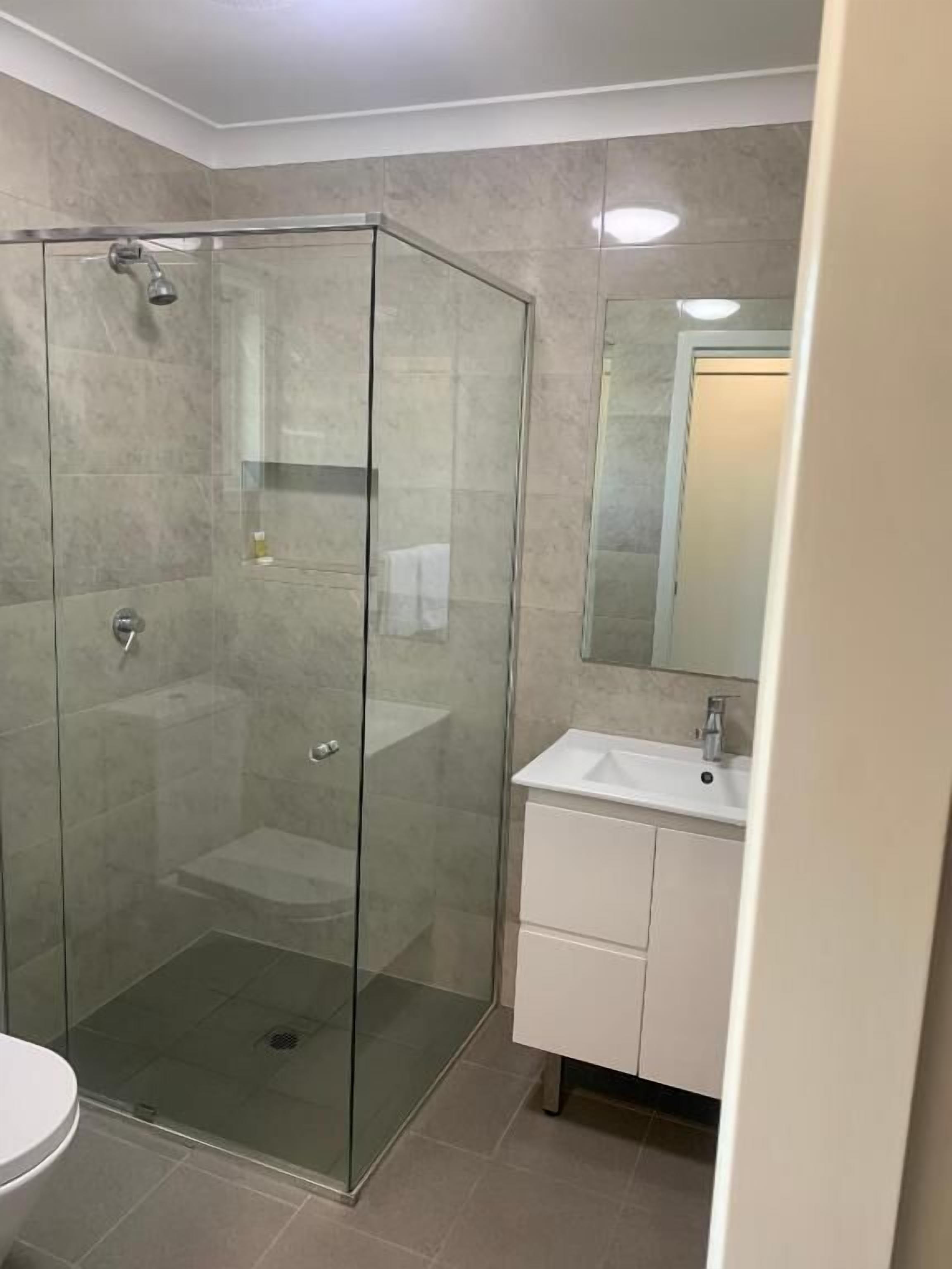 A bathroom with a glass-enclosed shower, a white sink, and a mirror above it.