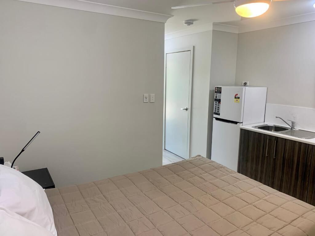 A hotel room with a bed, a kitchenette with a refrigerator, and a door leading to another room.