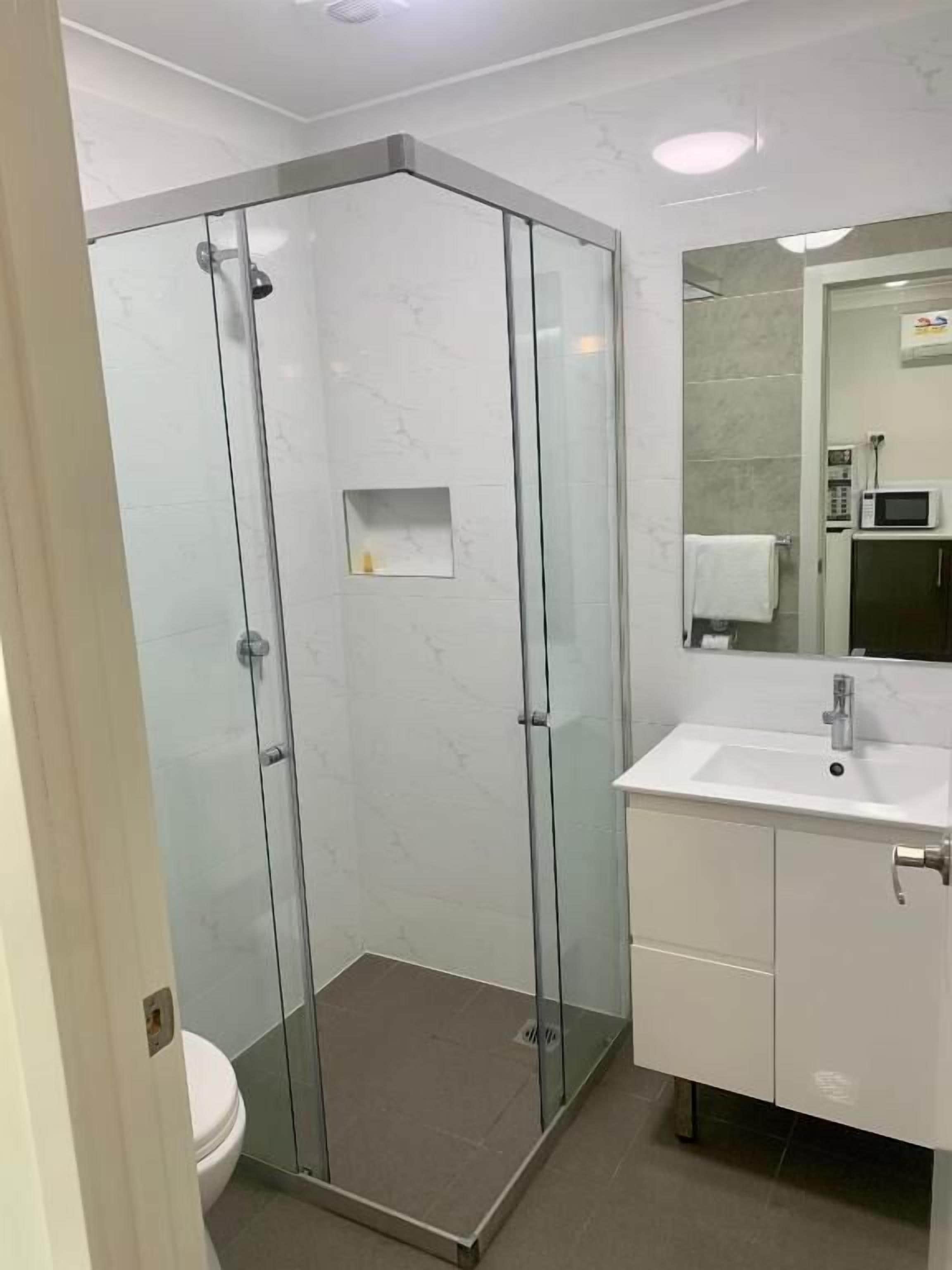 A modern bathroom with a glass-enclosed shower, a white sink, and a mirror above it.