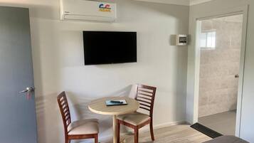 Quarto com televisão de tela plana na parede, uma mesa redonda com duas cadeiras e um ventilador de teto.