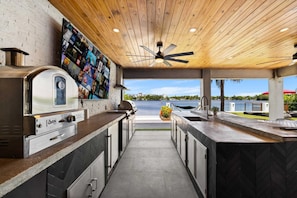 An outdoor kitchen with a grill, oven, and a wall-mounted TV.