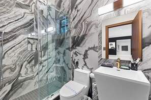 Ein modernes Badezimmer mit Marmorwand, einer Duschkabine aus Glas, einer Toilette und einem Waschbecken mit Spiegel.