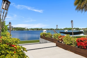 A waterfront patio with a view of a lake, surrounded by greenery and modern lamp posts.