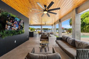 A covered outdoor lounge area with a ceiling fan, seating, and a wall with movie posters. - Star Villa | Opulent Waterfront Property (North Miami Beach)