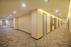 Un couloir d'hôtel avec des revêtements de sol en moquette, des portes et un éclairage encastré.