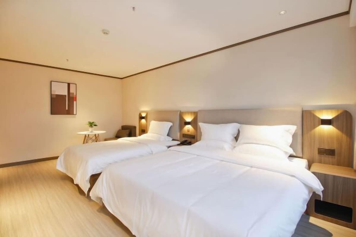 A modern hotel room with two beds, a small table with a plant, and wall-mounted lighting.