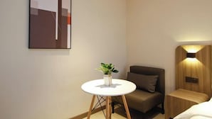 A modern hotel room with a bed, a small round table with a plant, a brown armchair, and a wall-mounted light fixture. - HanTing Hotel (Xi'an Bianjiacun Subway Station) (Xi'an)