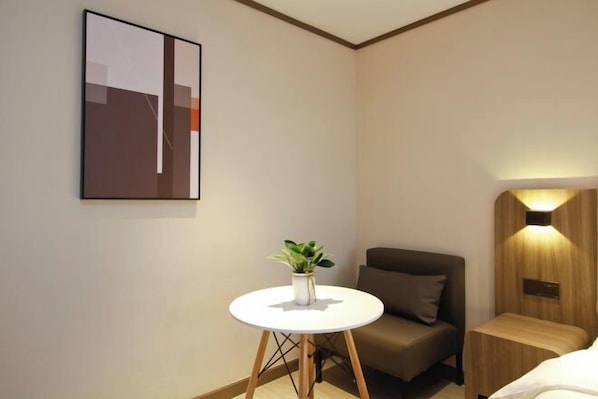 A modern hotel room with a single bed, a small round table with a plant, a brown armchair, and a wall-mounted light fixture. - Elong Anyun Hotel (Xi'an Northwest University Bianjiacun Subway Station) (Xi'an)
