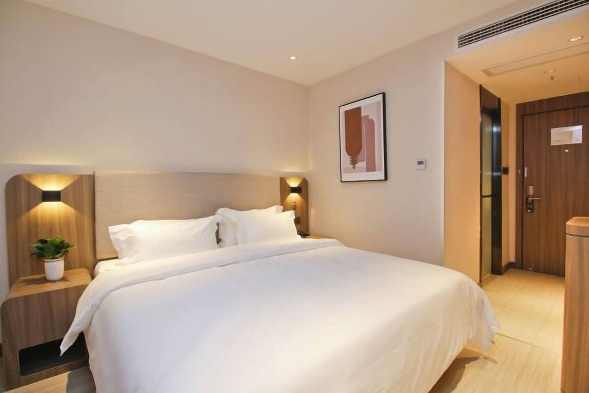 A hotel room with a bed, bedside tables, a wall-mounted light, a door, and a framed picture.