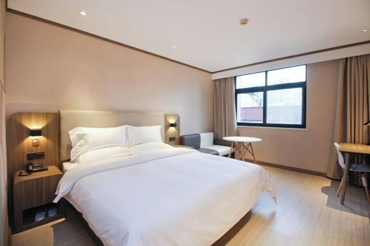 A hotel room with a large bed, bedside tables, a small round table, and a window with curtains.