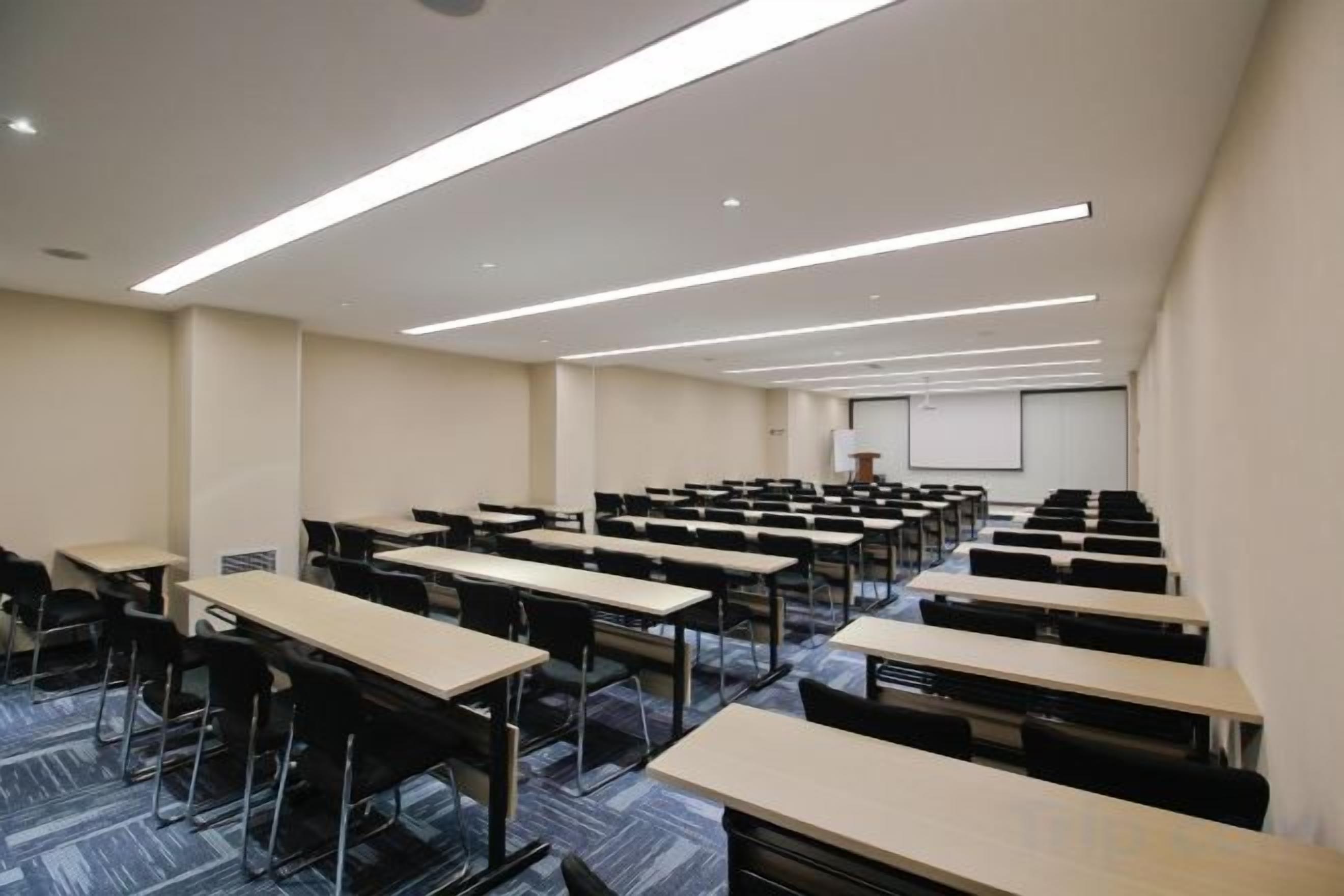 A conference room with rows of tables and chairs, a projector screen, and a whiteboard.